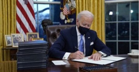 President Joe Biden wearing a face covering and signing a bill